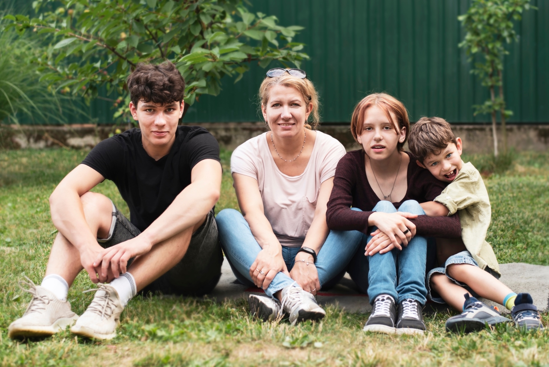 Happy woman with three children of different ages resting sitting on the grass, talking and smiling, posing to the photographer's father. Children enjoy communication with their mother