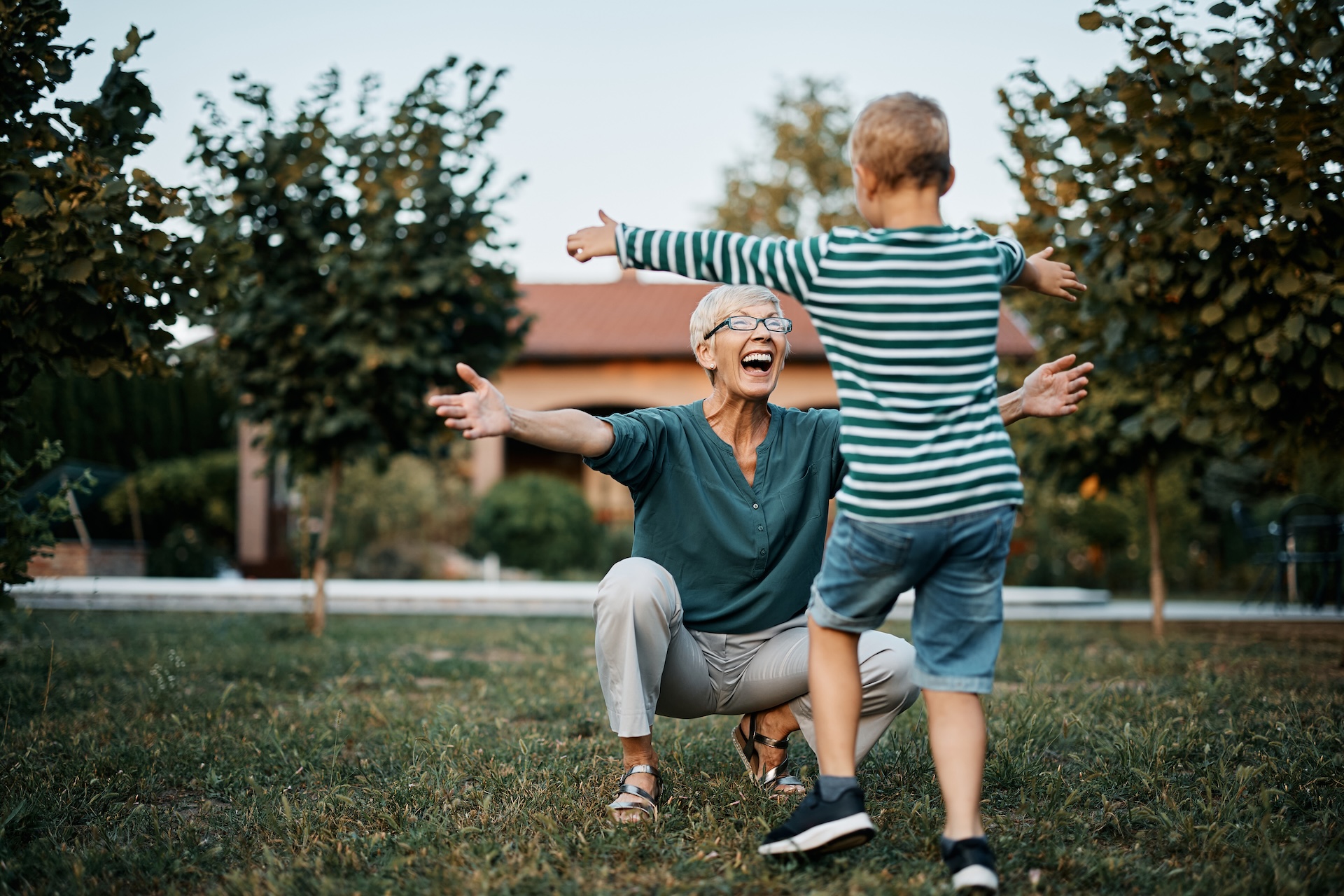 Happy senior woman greeting her son with arms outstretched in backyard.